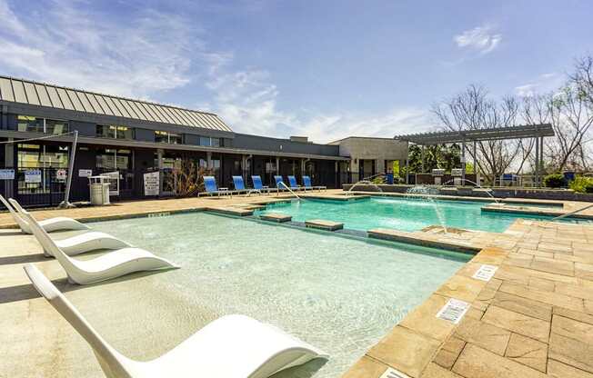 A pool area with sun loungers and a building in the background.