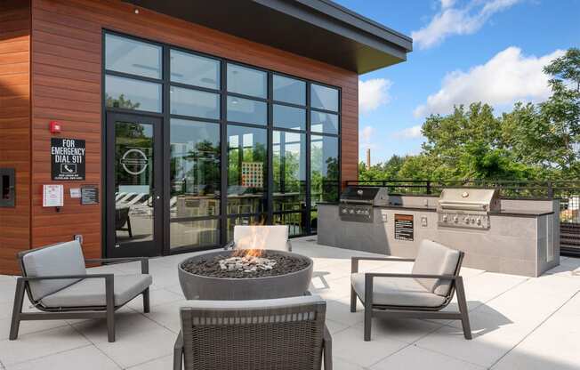 a patio with chairs and a fire pit in front of a building with large windows