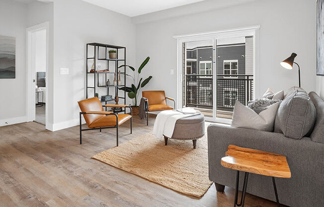 A living room with a grey couch, a brown chair, a white chair, a wooden table, a rug, and a plant.