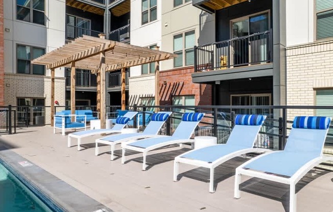 A poolside area with blue lounge chairs and a wooden pergola.