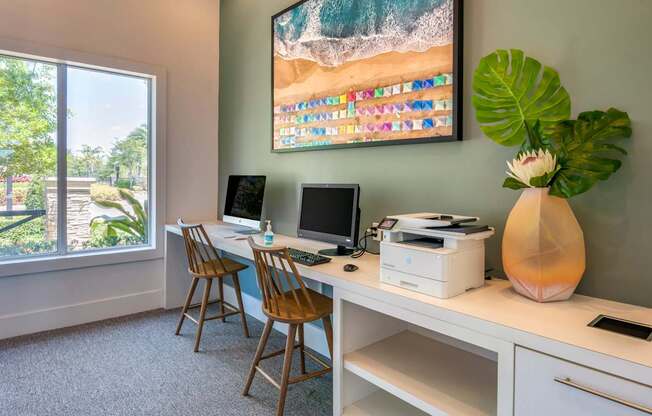 A room with a desk, chairs, and a large painting of a beach scene.