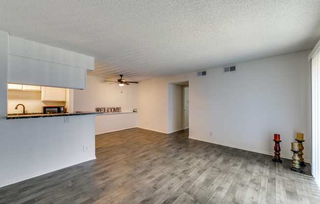 the living room and kitchen of an apartment with a hard wood floor and white walls