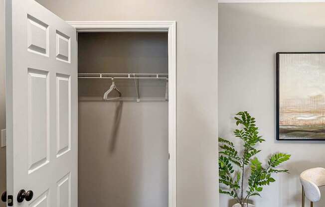 A white door with a black handle is open to a room with a plant and a painting.