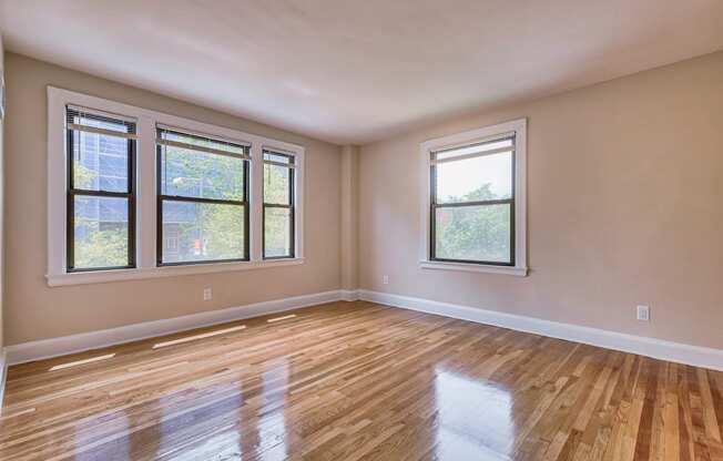 an empty living room with wood floors and three windows