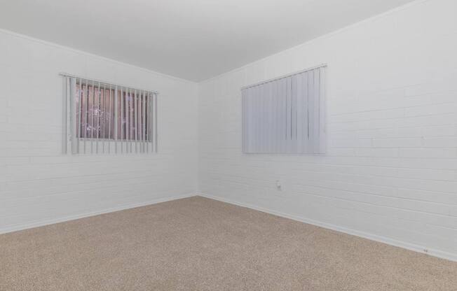 A room with a carpeted floor and two windows.