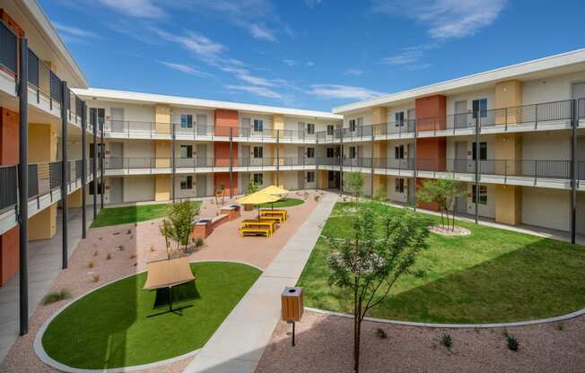 a courtyard with grass and tables and chairs in the middle of an apartment complex