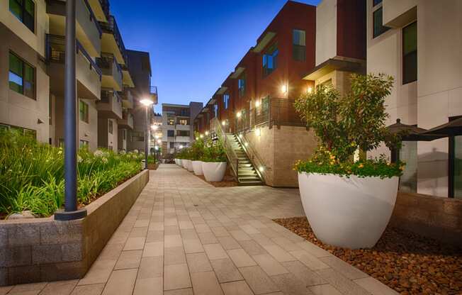 a picture of an apartment complex at night with the lights on and plants in the planters