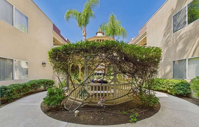 A tree-covered gazebo is in the middle of a courtyard.