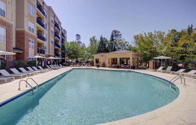 A large outdoor swimming pool surrounded by sun loungers and a building in the background.