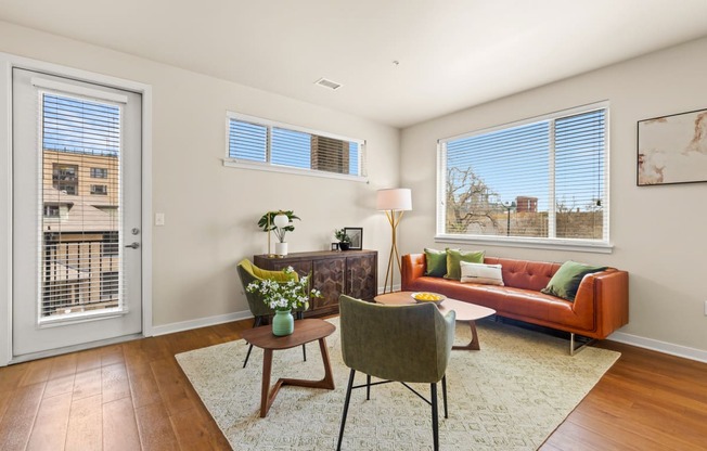 Spacious living room with a couch and chairs surrounding in natural light from the windows and door leading out to the balcony at Sylvan Uptown, Colorado