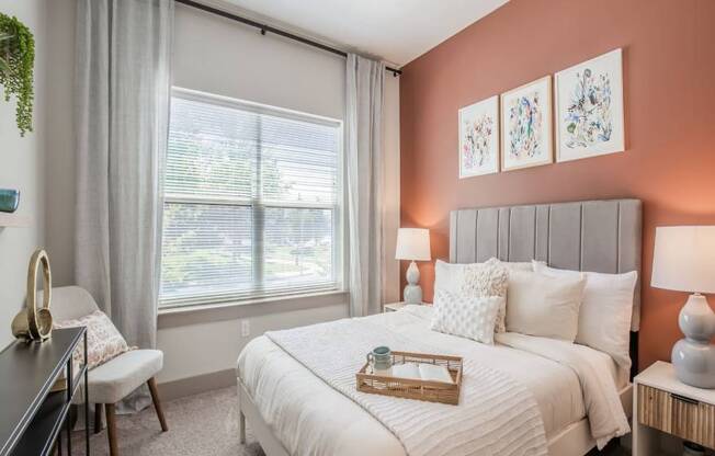 A bedroom with a large bed, a window with curtains, and a potted plant on the window sill.