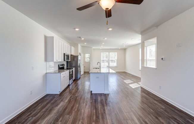 an empty living room with a ceiling fan and a kitchen