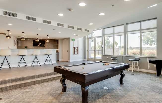 an open living room with a pool table and a bar with bar stools