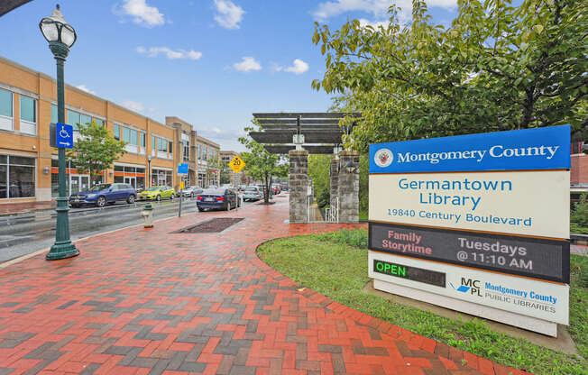 A sign for the Montgomery County Germantown Library is displayed on a brick walkway.