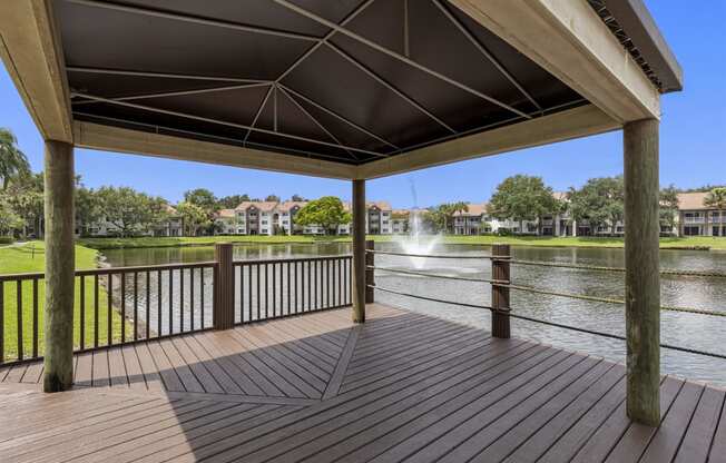 Covered deck area  with table and chairs overlooking community lake area with fountain feature