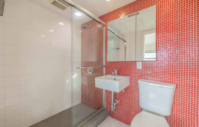 A red tiled bathroom with a toilet, sink, and shower.