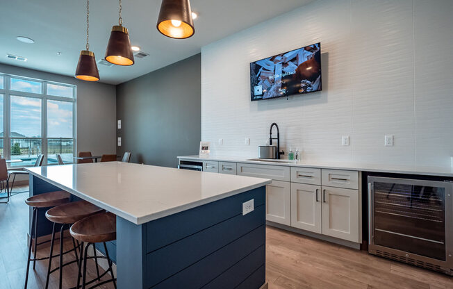 A modern community kitchen here at Van Buren East with a large island and bar seating. A beverage cooler, mounted TV, and nearby windows create a stylish, social, and inviting gathering space.