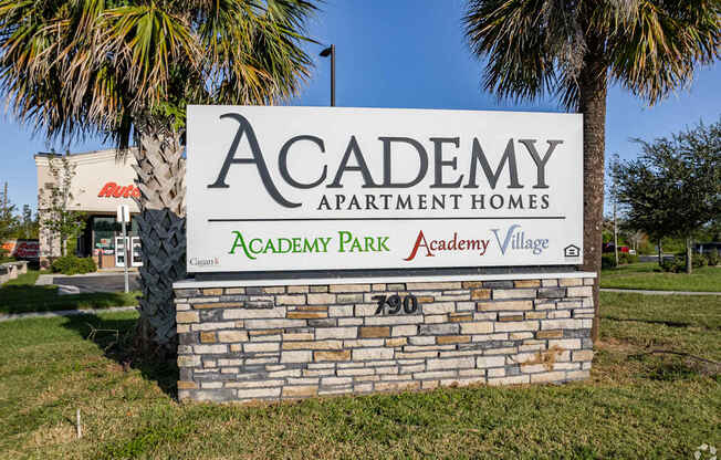 A stone sign for Academy Park Apartment Homes stands in front of a palm tree.