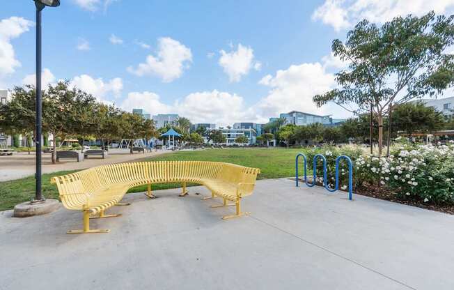 A yellow bench sits in a park with a blue pole behind it.