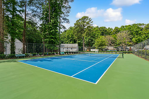 a tennis court with blue and green turf and a fence and trees at Lake Johnson Mews, Raleigh