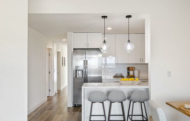 a kitchen with white cabinets and a bar with three stools