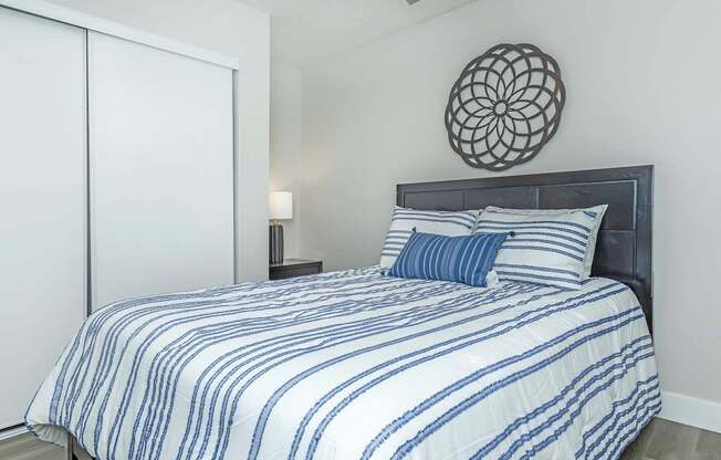 A bed with a blue and white striped comforter and two matching pillows sits in a room with a ceiling fan and a wall-mounted light fixture.