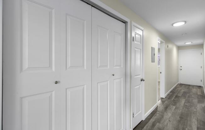 a long hallway with white closet doors and white walls at Swiss Gables Apartment Homes, Kent, WA