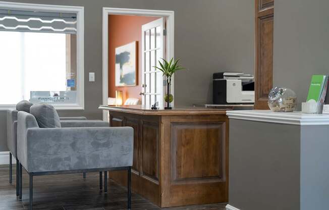 A grey chair sits in front of a desk with a printer on it.