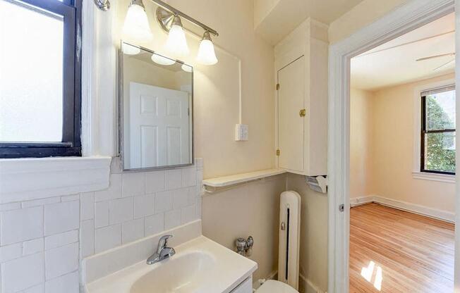 bathroom with vanity, mirror, toilet and view of bedroom at the klingle apartments in washignton dc