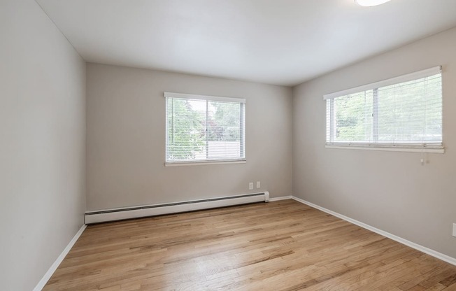 an empty bedroom with wood floors and two windows