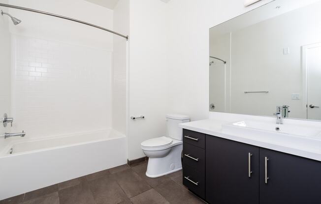 bathroom with white counter, large mirror and white tub and toilet