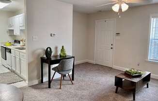a living room with a ceiling fan and a kitchen in the background