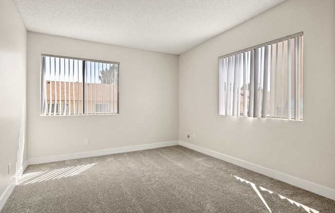 an empty living room with two windows and carpeting