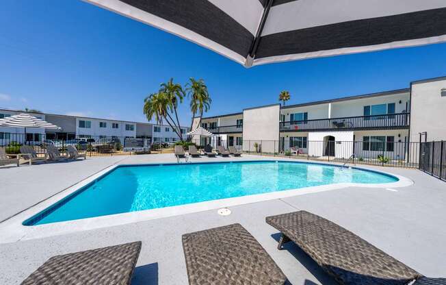 A swimming pool with sun loungers and a building in the background.