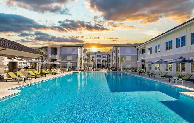 A large swimming pool surrounded by lounge chairs and buildings in the background.