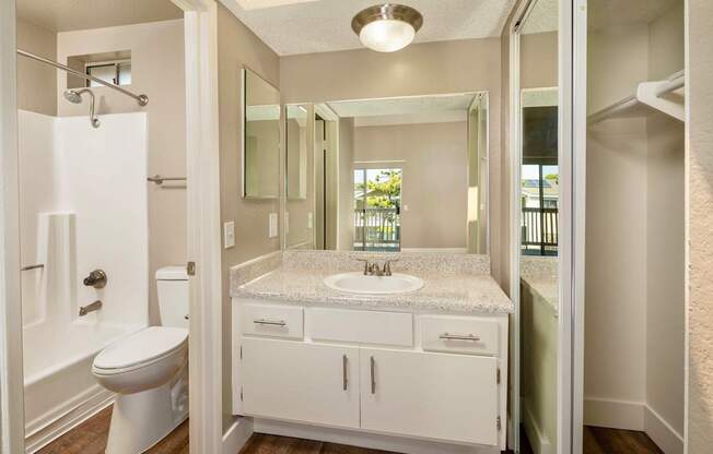 A bathroom with a toilet, sink, mirror and closet.