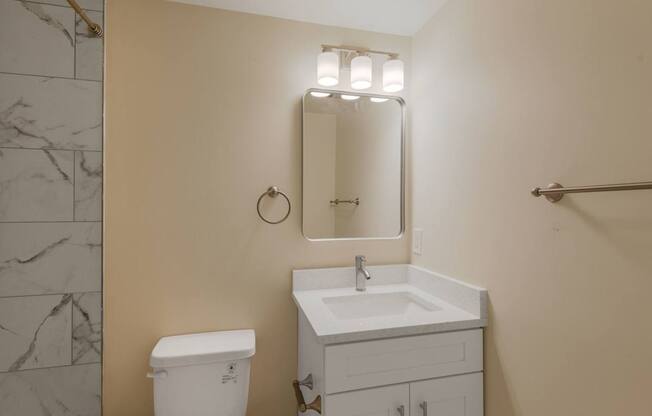 A bathroom with a toilet, sink, mirror and a towel bar.