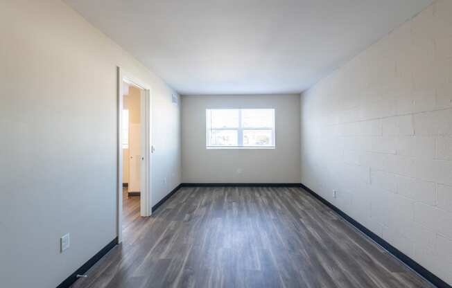 the living room of an empty apartment with wood flooring and a window