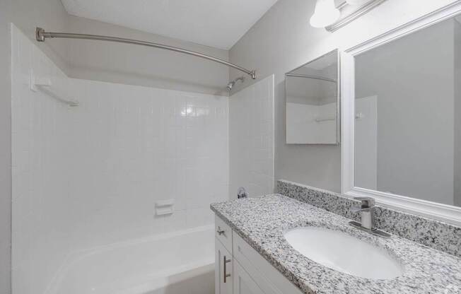 A white bathroom with a granite countertop and a white tub.
