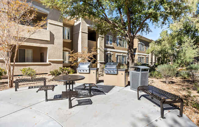 A patio with a table and chairs is surrounded by trees and a building.