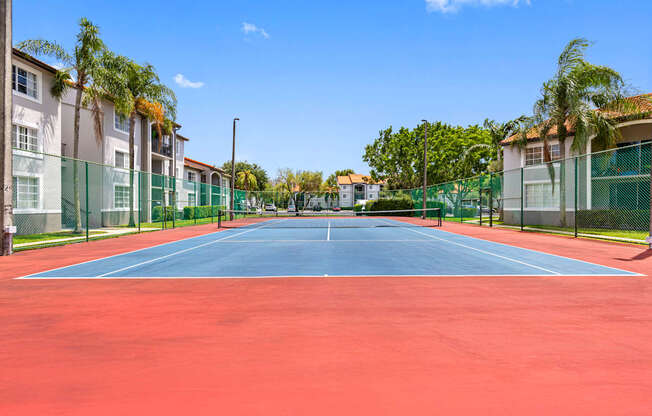 A tennis court with a red surface and a green fence surrounding it.