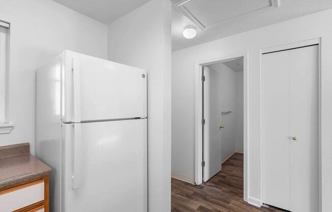 a white kitchen with a refrigerator and a door to a hallway