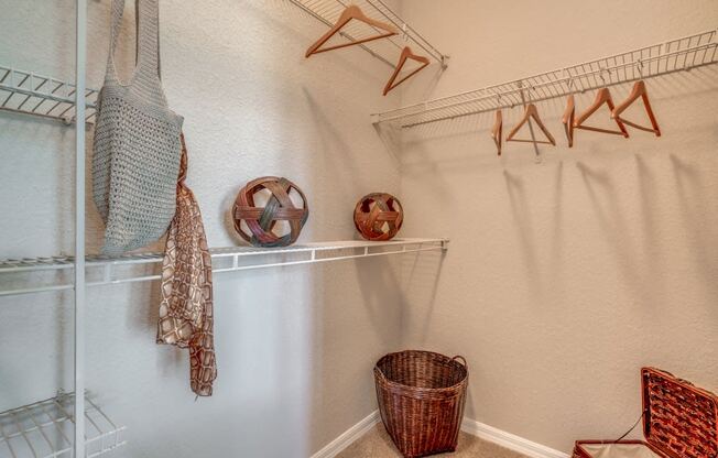 Furnished model walk-in closet with hangers, baskets and hamper.