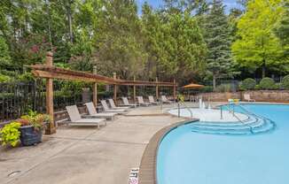 a swimming pool with chairs around it and trees in the background