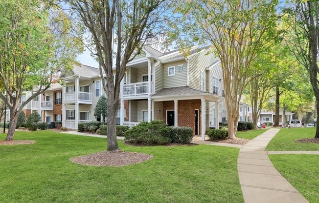 the view of two story apartment buildings with trees and a sidewalk