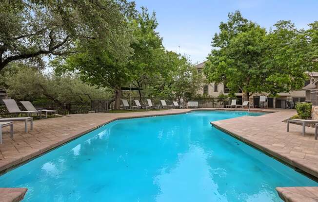 A large swimming pool surrounded by trees and lounge chairs.