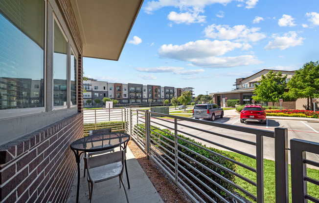 A balcony with a table and chairs overlooks a street with cars and buildings.