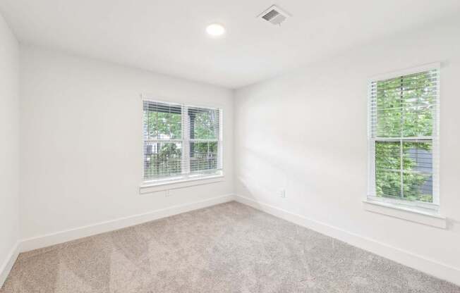 A bed room with a carpeted floor and two windows.
