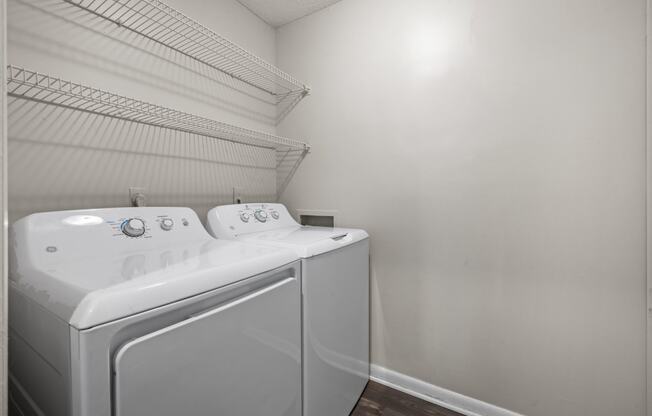 a washer and dryer in a laundry room with white walls and a shelf