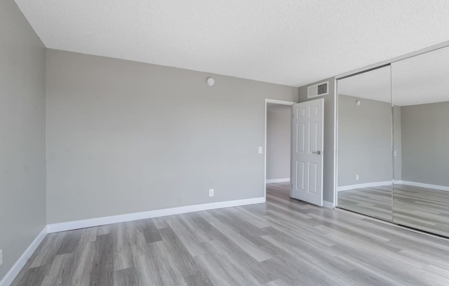 the spacious living room of an apartment with a door to the bedroom